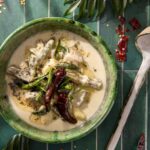 A green bowl with creamy coconut soup and veggies inside it.