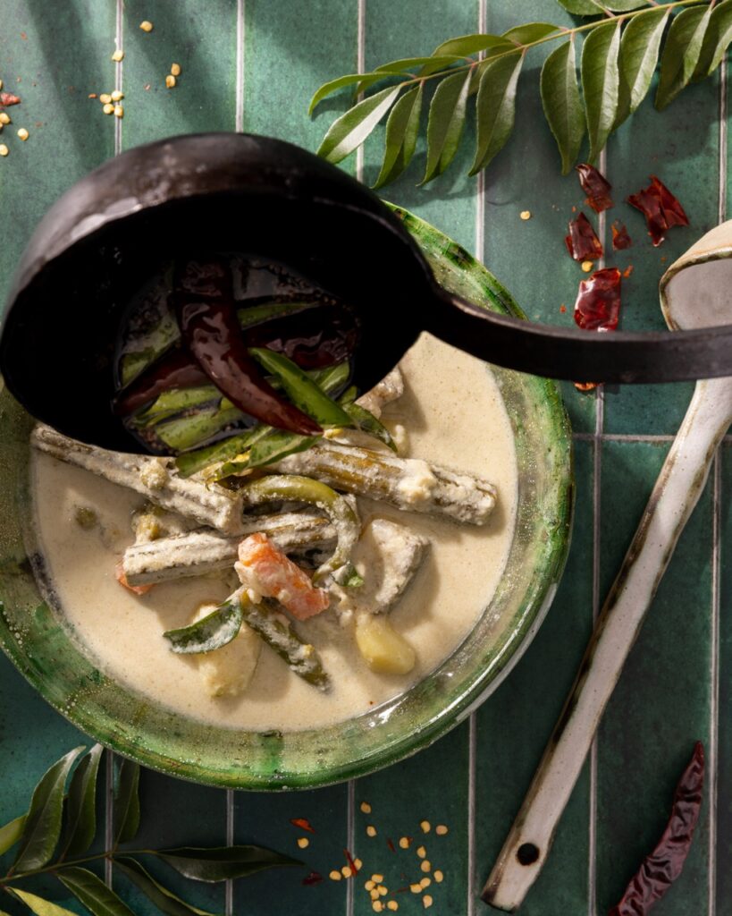 Laddeling vegetables into a green bowl with a creamy soup.