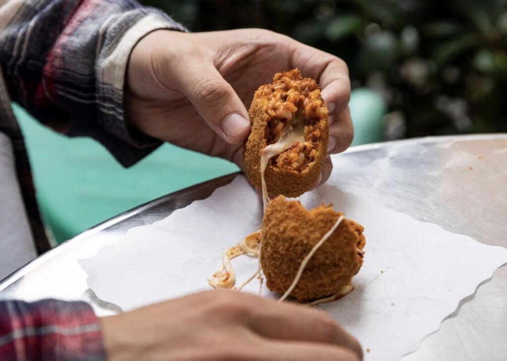A person pulls apart a deep fried ball of cheese.