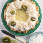 A kiwi-coconut cream pie sits on a green plate with whipped cream, shredded coconut, and kiwi slices on top.