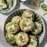 A green plate full of Kiwi Matcha White Chocolate Cookies with a cube of dried kiwi on top of each.