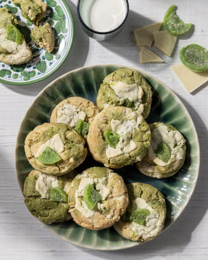 A green plate full of Kiwi Matcha White Chocolate Cookies with a cube of dried kiwi on top of each.