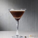 Miranda's espresso martini in a tall glass with gold leaf coffee beans on the white table below it.