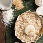 A palitaw chewy rice cake sits in a white bowl of coconut flakes with a coconut and other ingredients in the top left corner.