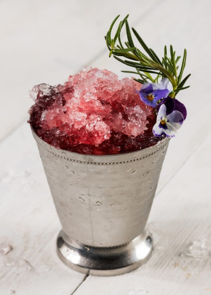 A pomegranate mint julep in a silver tin julep cup with crushed ice and a sprig of rosemary.