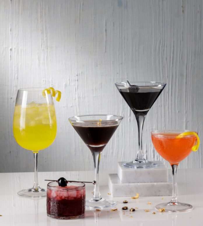 Five cocktails for The Devil Wears Prada 2 sit on a white table in tall and short glasses and various colors.