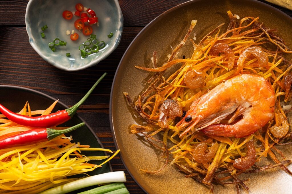 A brown plate with a filipino fritter of julienned vegetables with dried shrimp and one big prawn on top.