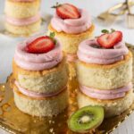 Three mini personal two-layer vanilla cakes with strawberry buttercream and kiwi jam in between the layers and a half strawberry on top.