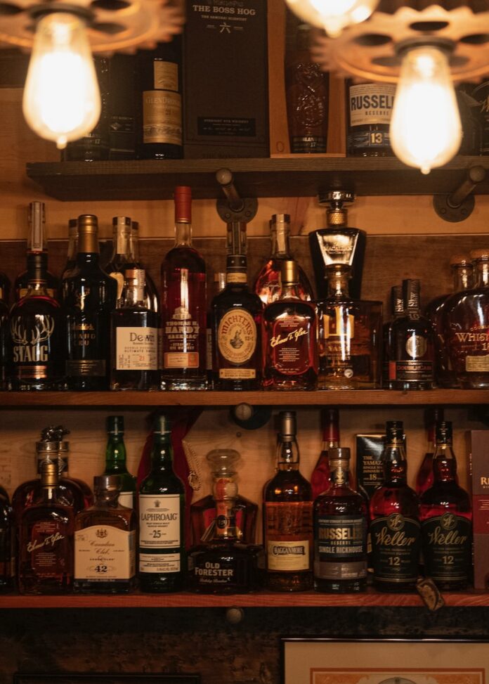 Two selves full of bottles of Scotch sit below two antique light bulbs behind a bar.