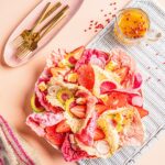 A bowl full of pink radichio and strawberries with a pink peppercorn vinaigrette in the upper right corner and gold silverware in the left.