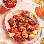 A pink plate full of Strawberry Balsamic Glazed Chicken Wings with a bowl of the sauce in the upper left corner.