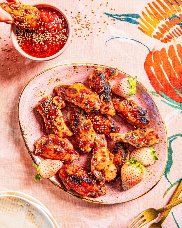 A pink plate full of Strawberry Balsamic Glazed Chicken Wings with a bowl of the sauce in the upper left corner.