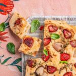 Two small slices of strawberry focaccia taken out of a whole loaf on a pink surface.