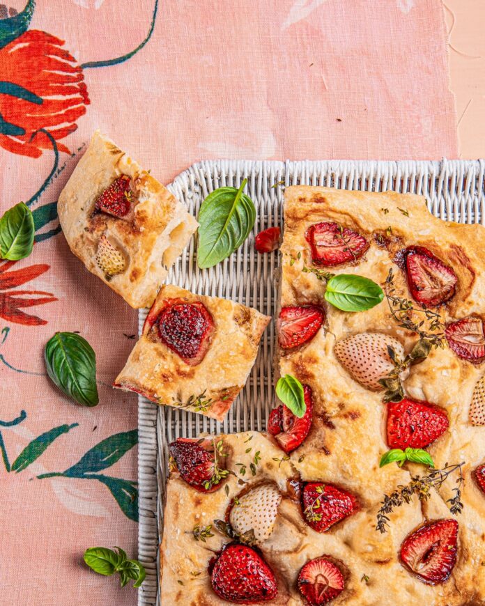 Two small slices of strawberry focaccia taken out of a whole loaf on a pink surface.