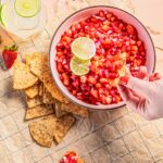 A bowl full of strawberry rhubarb salsa as a person dips a tortilla chip into it.
