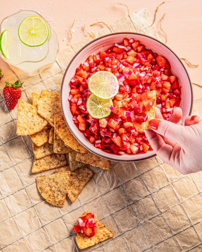 A bowl full of strawberry rhubarb salsa as a person dips a tortilla chip into it.
