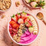 A Strawberry Smoothie Bowl in pink color with sliced strawberries, bananas, goji berries, and granola on top.