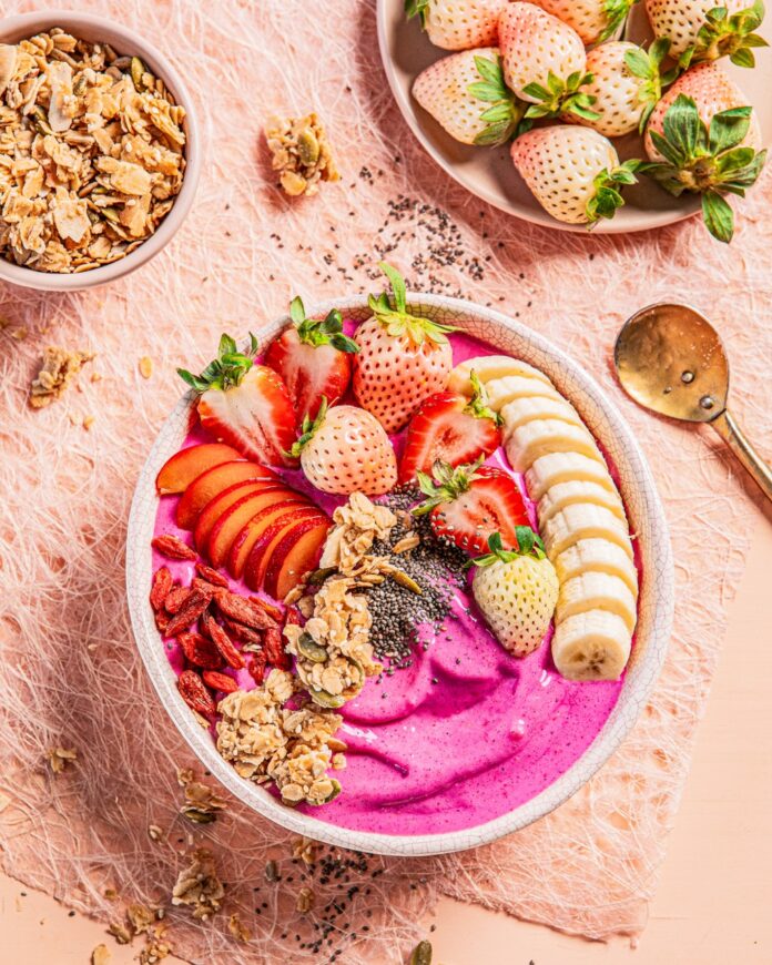 A Strawberry Smoothie Bowl in pink color with sliced strawberries, bananas, goji berries, and granola on top.