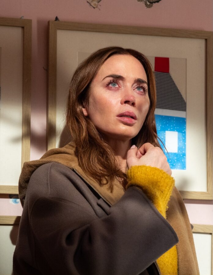 Emily Blunt with teary eyes looking up at the sky in her home.