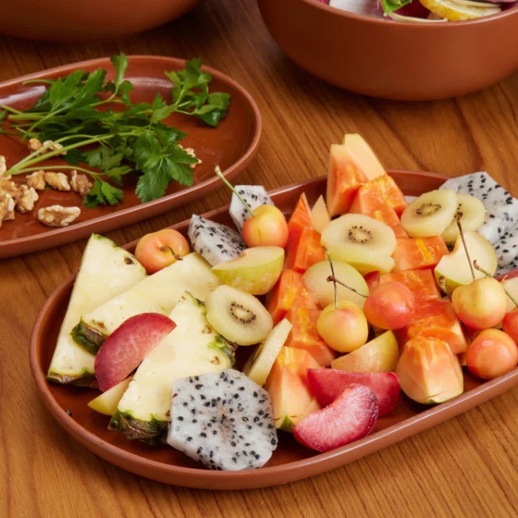 Two brown platters with fruit and vegetables.