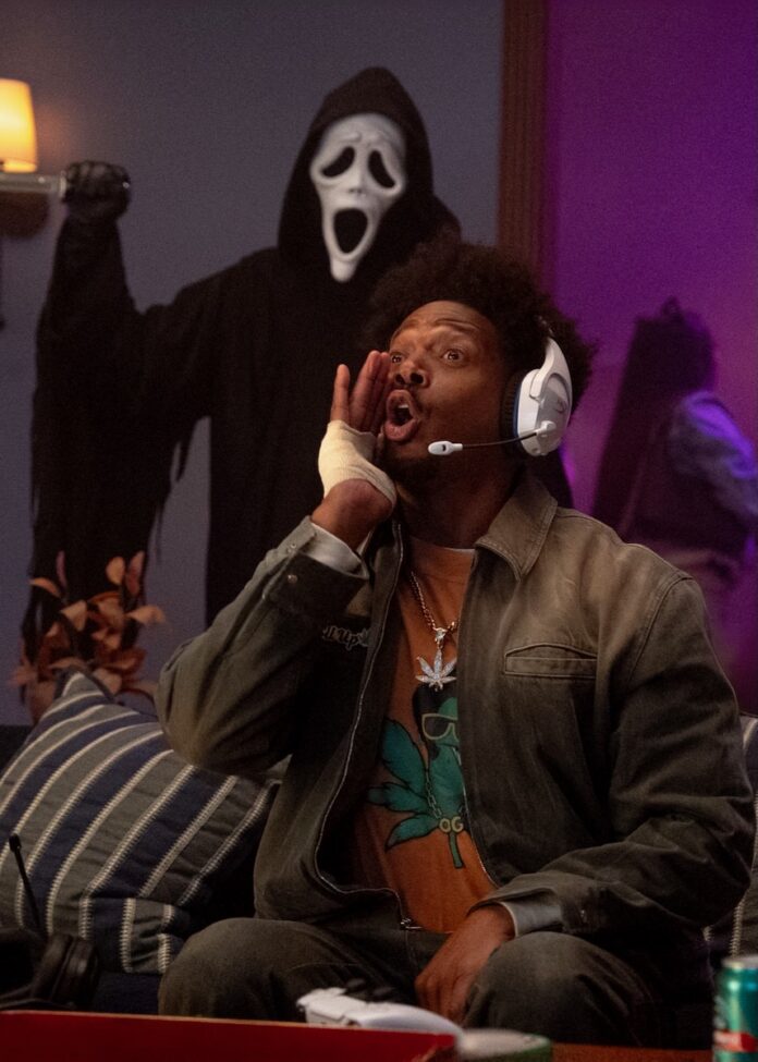 A man playing a game and hollering while the ghost face killer stands behind him with a knife.