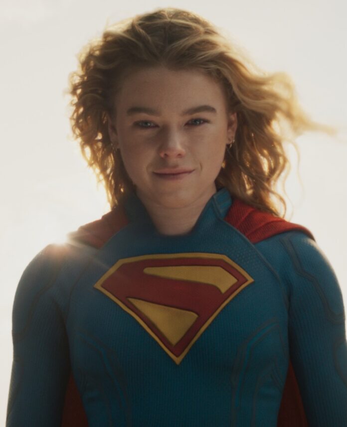 Supergirl stands in her costume with her hair blowing back and the sun glowing around her.