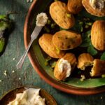 Freshly baked green chile corn madeleines topped with smoked honey butter on a rustic plate.