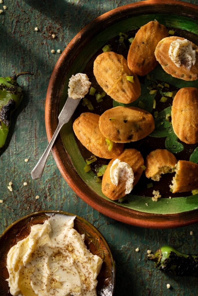 Freshly baked green chile corn madeleines topped with smoked honey butter on a rustic plate.