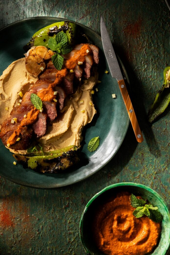 Sliced roasted lamb loin over chickpea purée drizzled with red green chile harissa and garnished with fresh mint.