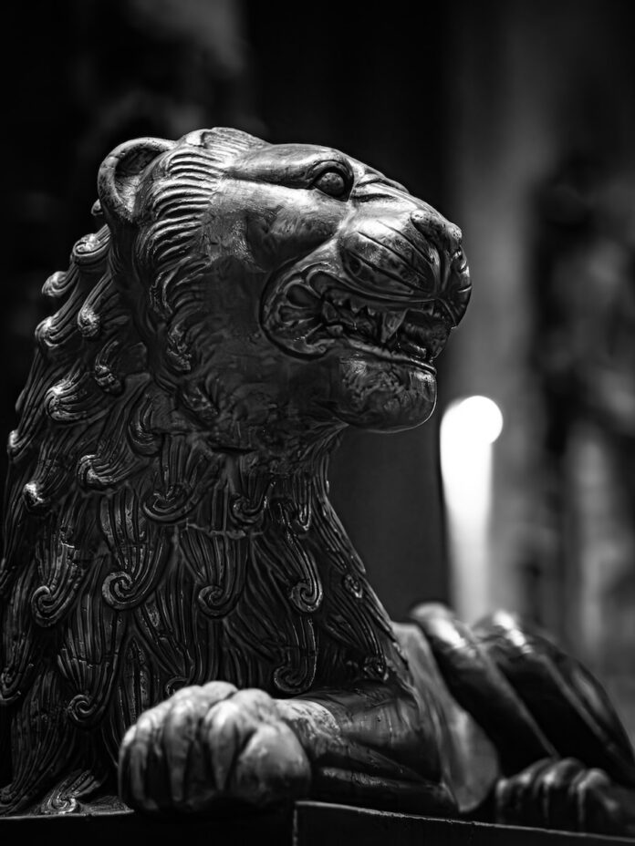 A black and white photo of a lion statue laying down.