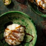 Vanilla bean panna cotta topped with espresso green chile caramel drizzle and shaved chocolate in a green bowl.