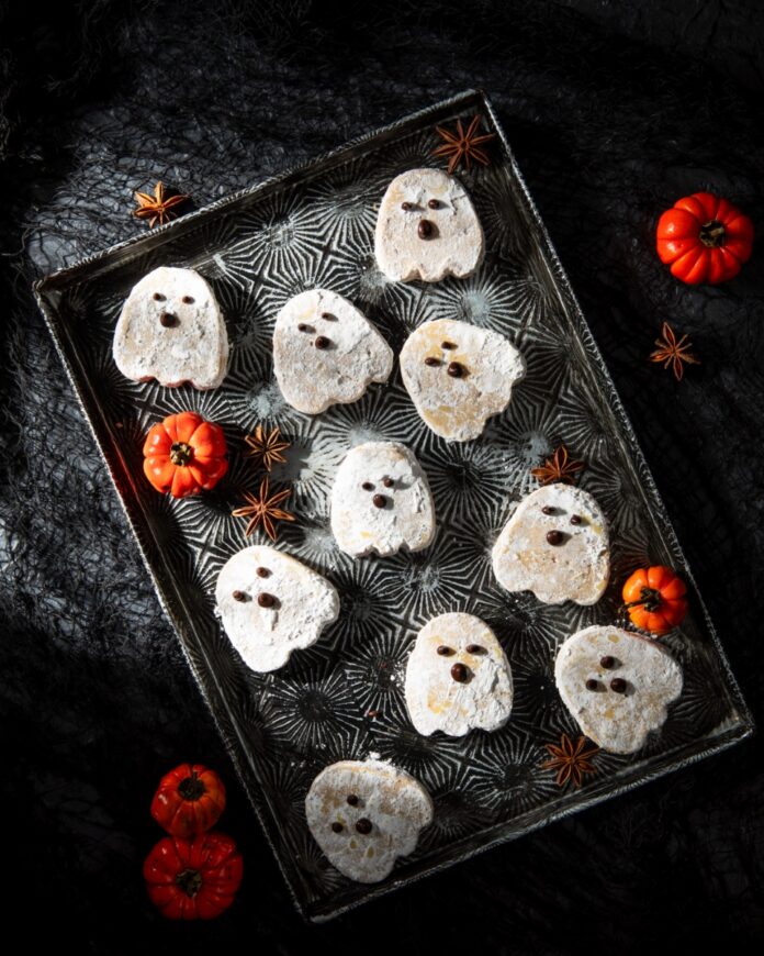Ghostly Pumpkin and Brown Butter Shortbread Cookies TABLE Magazine Ghost-shaped pumpkin brown butter shortbread cookies dusted with powdered sugar and decorated with melted chocolate faces, arranged on a vintage tray with mini pumpkins and star anise.