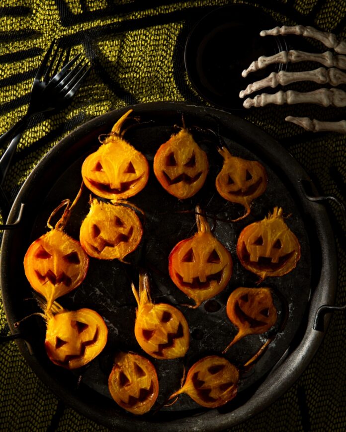 Jack O’Lantern Roasted Beets With Apple Cider Glaze TABLE Magazine A tray of roasted golden beet halves carved with jack o’lantern faces and drizzled with apple cider glaze on a platter.
