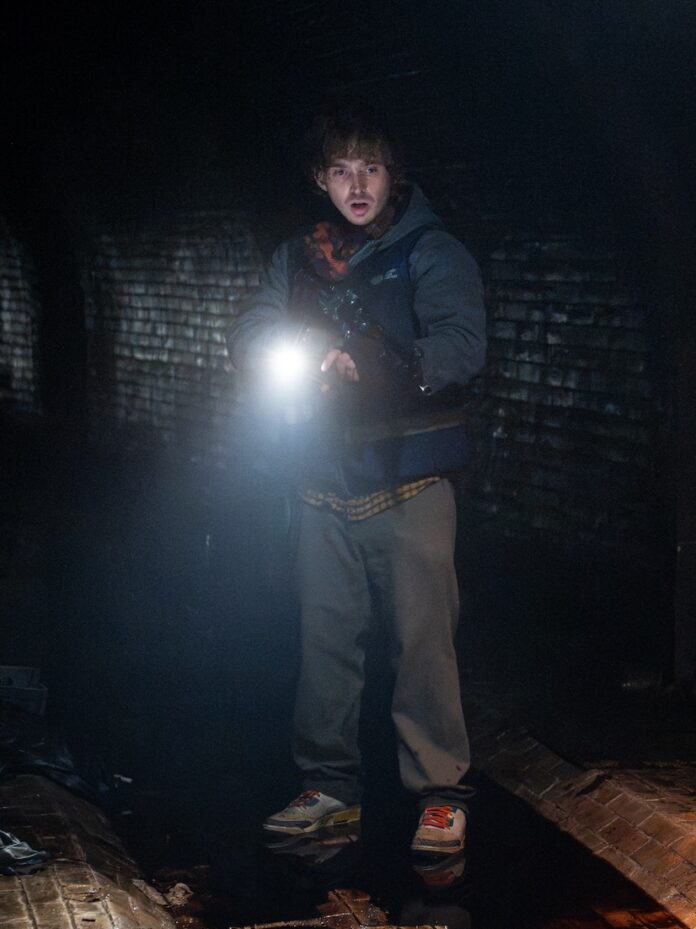 Resident Evil TABLE Magazine 2 Austin Abrams traveling through a bloody dark tunnel with a flashlight in Resident Evil.