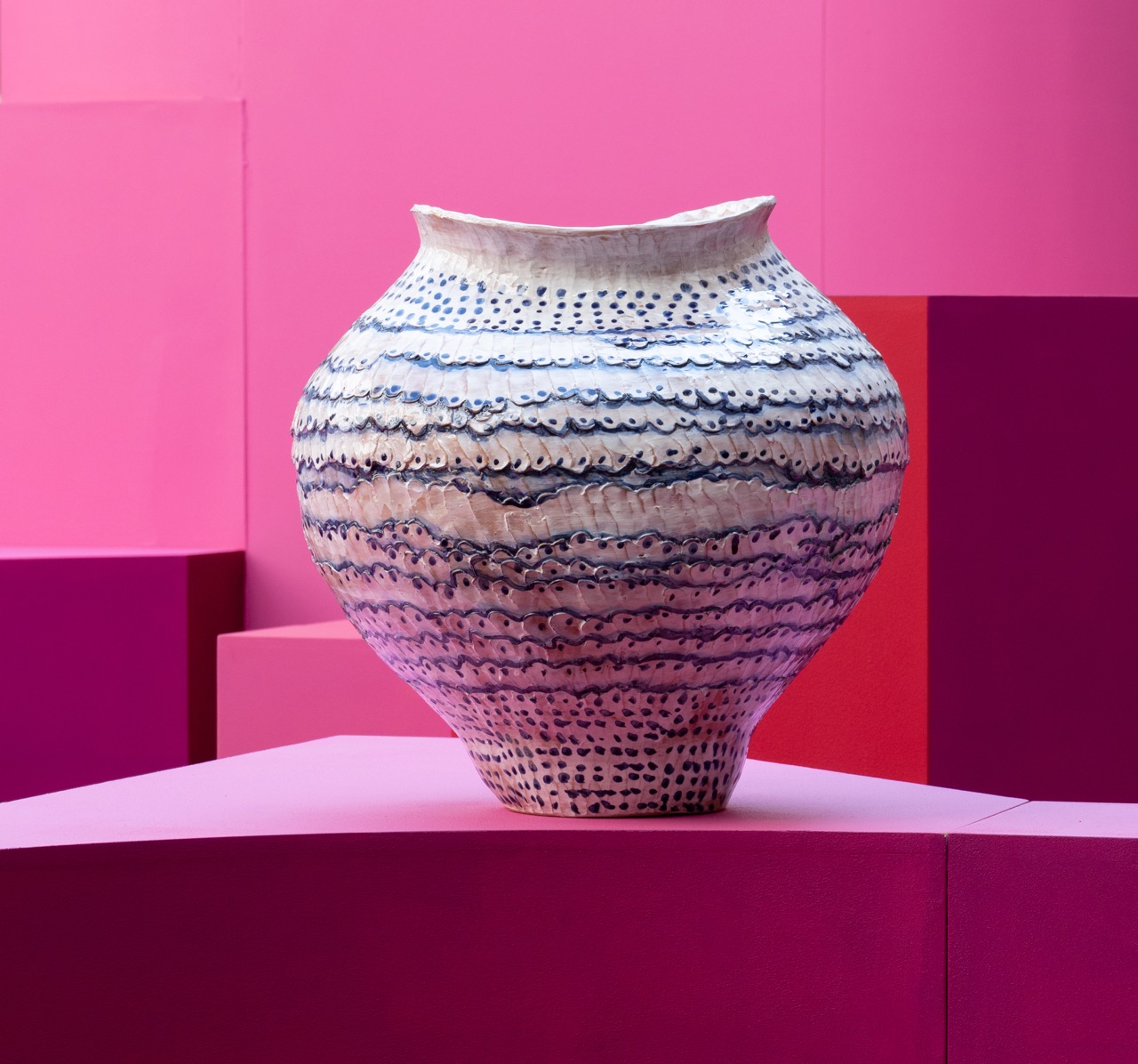 A white and black pattern Unda Vases by Onofrio Acone on a pink stand with a pink background.
