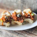 Three buffalo turkey sliders on a white plate and wood table.