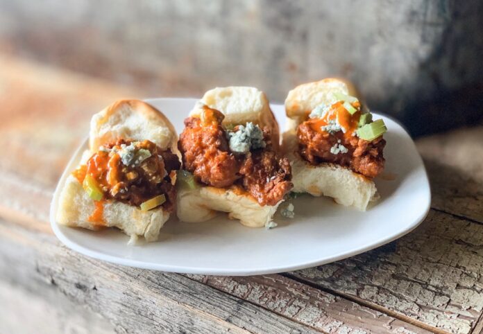 Three buffalo turkey sliders on a white plate and wood table.