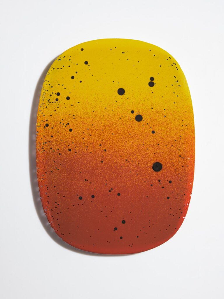 An orange and yellow ombre oval with black dots in random spots. 