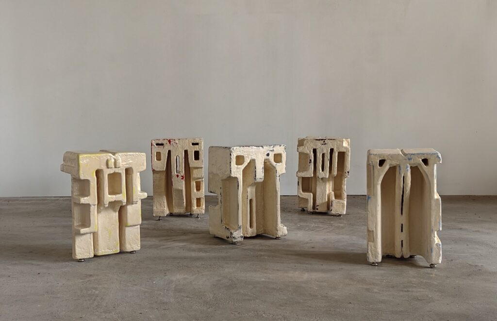 Multiple large beige block structures by Studio Manon Stoeltie against a grey background.