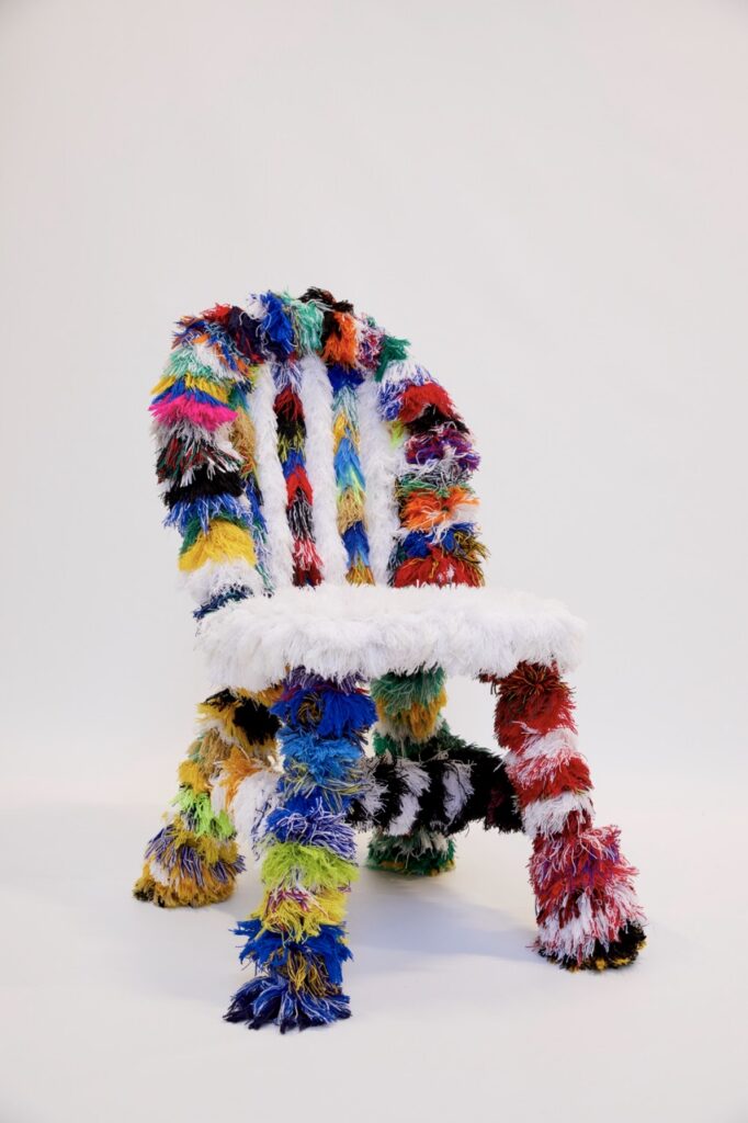 A dining chair covered in colorful fringe with white fringe on the seat.