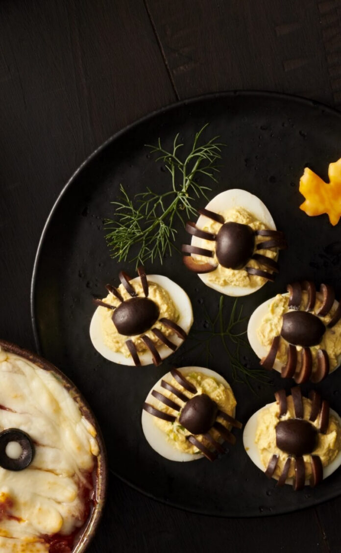 Deviled eggs topped with black olive spiders on a Halloween serving platter.