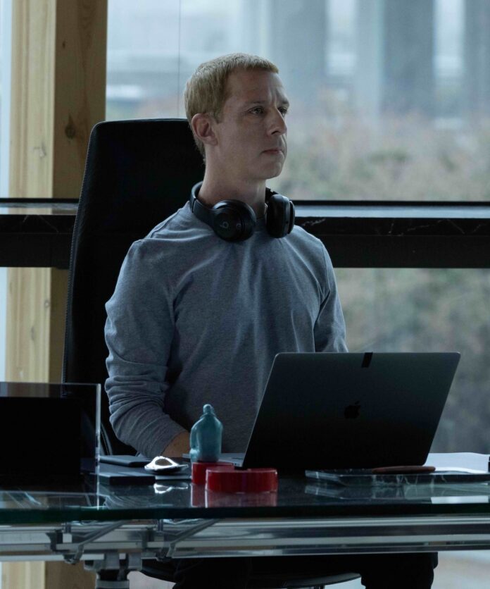 Mark Zuckerberg (Jeremy Strong) in Columbia Pictures' THE SOCIAL RECKONING. Jeremy Strong sits in an office chair as Mark Zuckerberg with headphones around his neck and a laptop in front of him.
