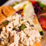 A croissant with turkey salad sandwich filling between its layers and a small salad behind it.