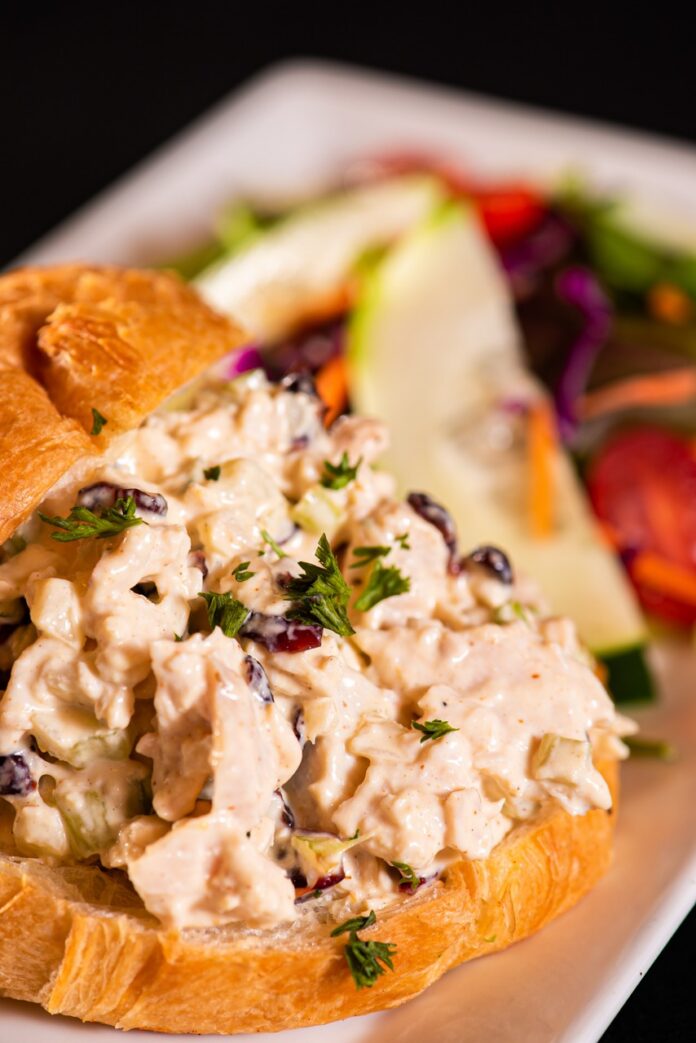 A croissant with turkey salad sandwich filling between its layers and a small salad behind it.