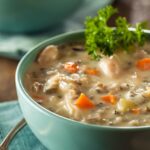 A blue bowl full of turkey and vegetable soup with a leafy green garnish and another bowl in the background.