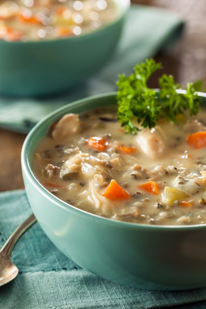 A blue bowl full of turkey and vegetable soup with a leafy green garnish and another bowl in the background.