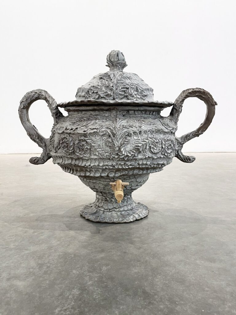 A stone grey pot with handles that curl against it by Buro Mesnildot.